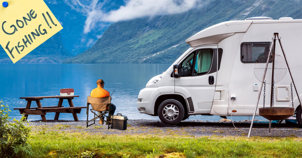 A man sitting outside of his RV fishing at a mountain lake