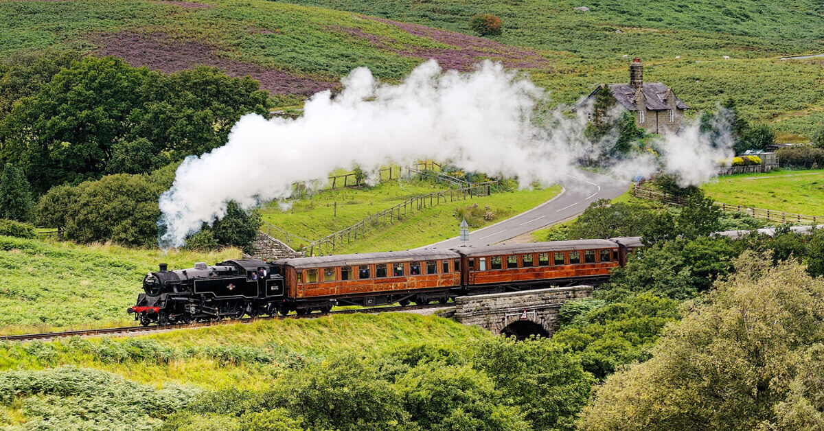 A Steam Enging pulling a passenger train thourgh a green valley