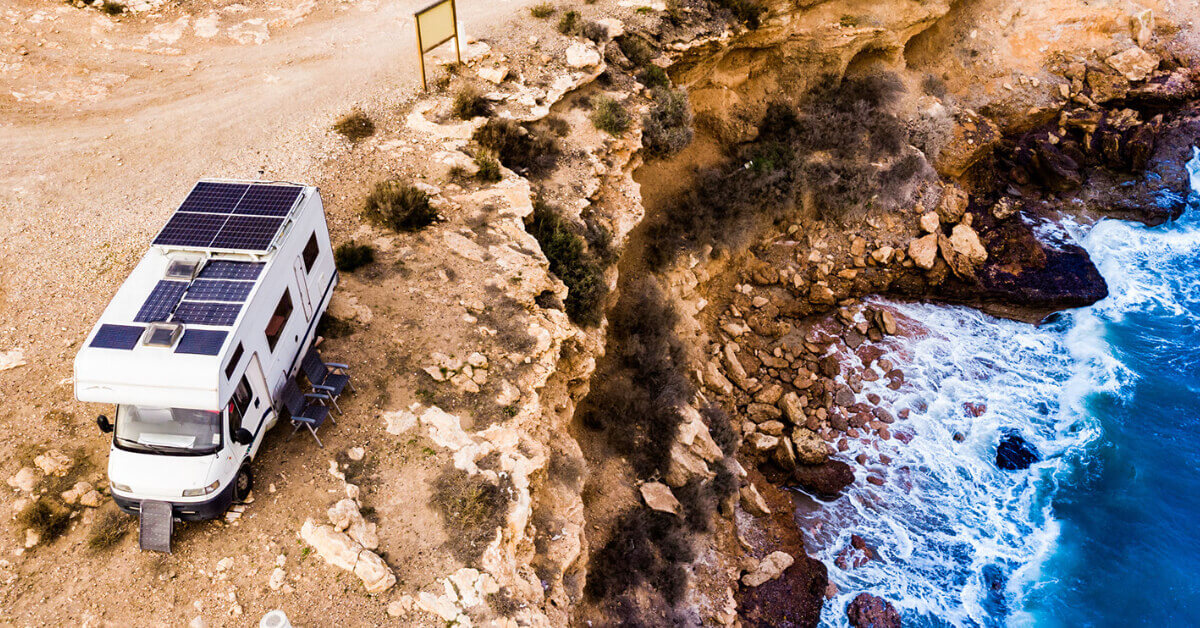 An RV with solar panels parked on a cliff overlooking the ocean