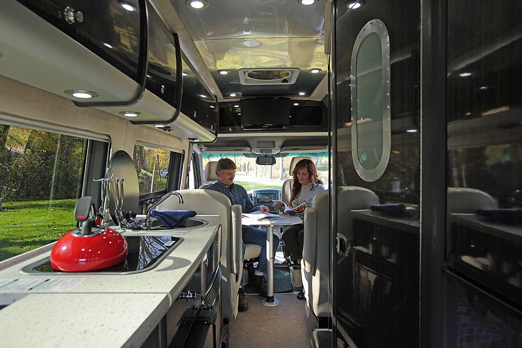 Couple sitting at table reading magazines inside of a Class B Motorhome