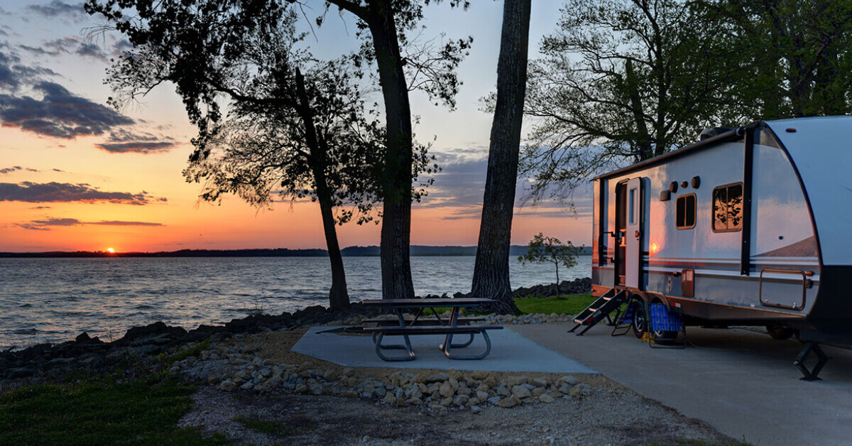 A Travel Trailer in a campground overlooking a lake at sunset