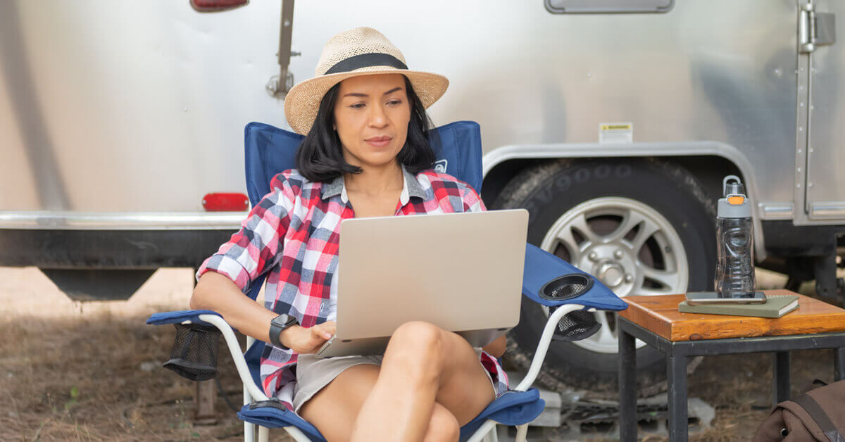 a woman sitting outside of her RV while cruising the internet on laptop