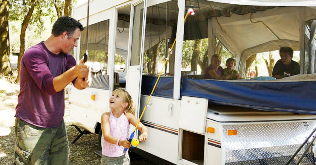 A father and daughter standing outside of their Tent Trailer holding their fishing rods