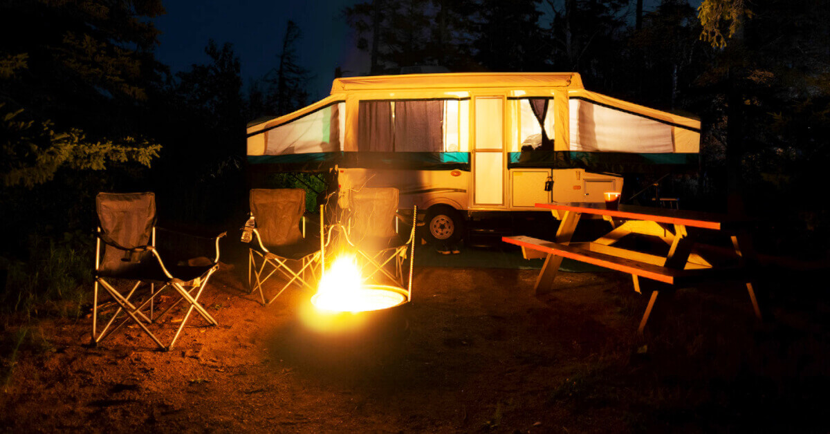 A Tent Trailer at a campground at night with a campfire