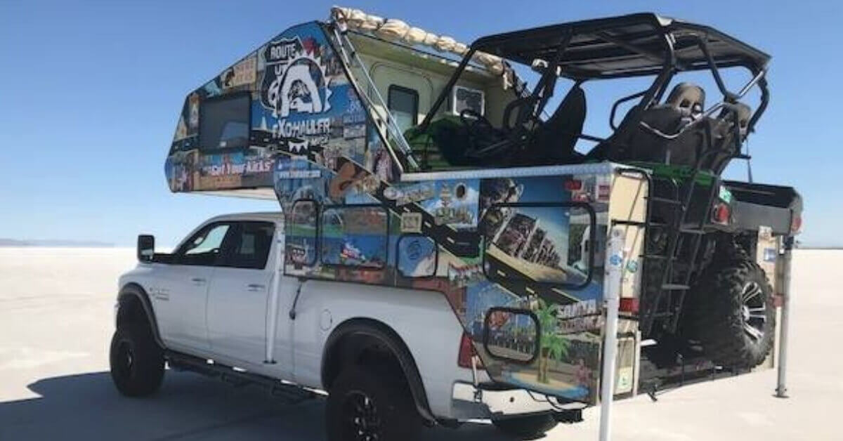 A pickup truck with an EXO-Hauler toy hauler camper parked on some desert dunes