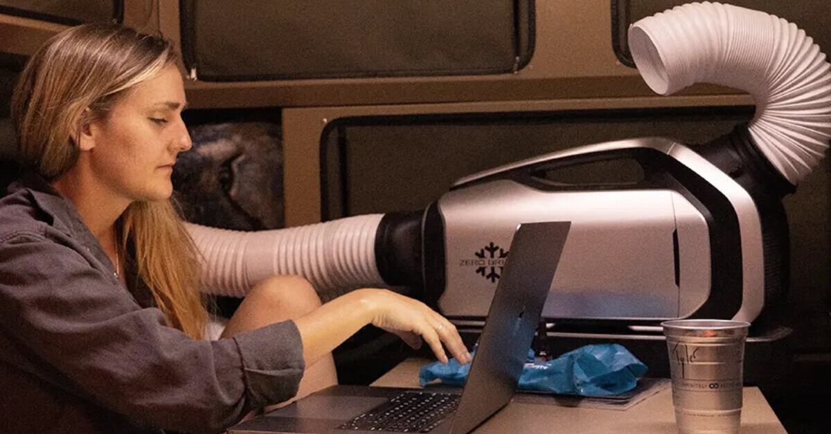 A Women using a computer in her Travel Trailer on a sweltering summer night, but staying cool by using her Zero Breeze Mark 2 Portable AC